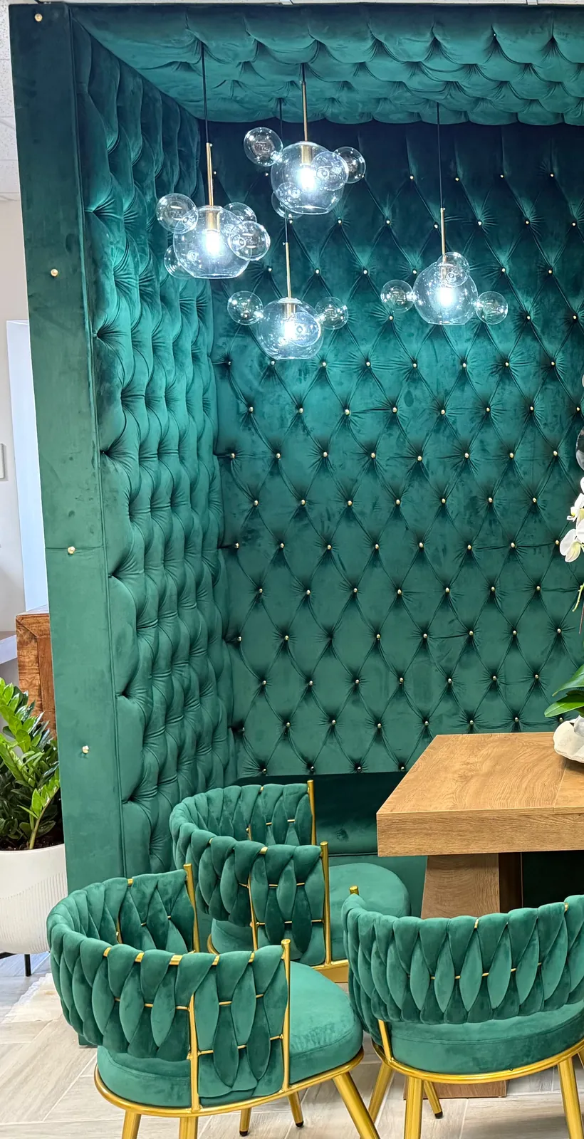 Floor-to-ceiling tufted wall in emerald velvet framing a dining booth with green chairs