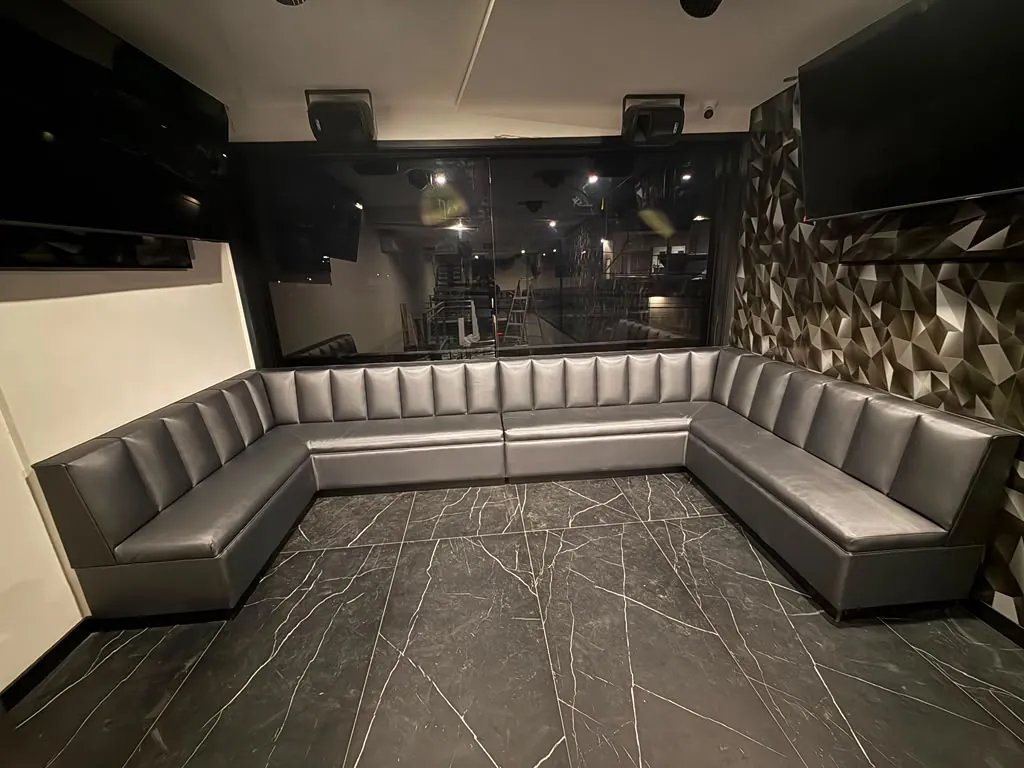 U-shaped gray metallic vinyl booth with channel back in a VIP room with dark marble floor